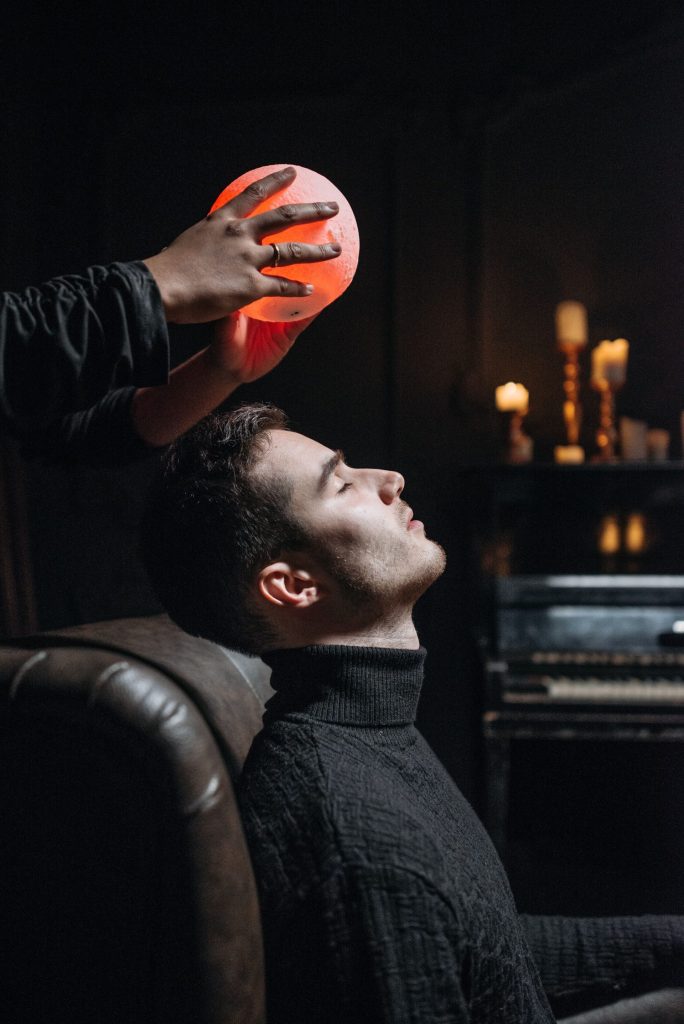 A person immersed in a mystical seance, holding a glowing orb indoors with candles.